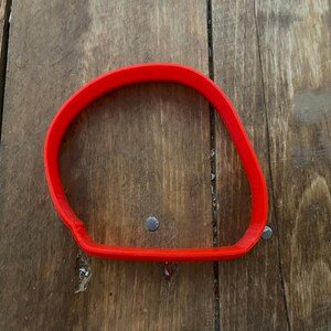 Peut inclure: Emporte-pièce en plastique rouge vif en forme de rectangle arrondi. Le découpoir est fait d'une seule pièce de plastique et repose sur une surface en bois. Le découpoir mesure environ 10 cm de long et 7,6 cm de large.
