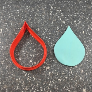 Puede incluir: Dos cortadores de galletas con forma de lágrima. Uno es rojo y el otro es azul claro.