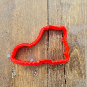 Puede incluir: Un cortador de galletas de plástico rojo con forma de bota.