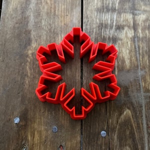 May include: A red plastic snowflake cookie cutter. The cutter is on a wooden surface.