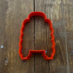 May include: Orange plastic cookie cutter shaped like a person with a wavy hair style.