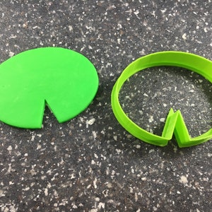 Könnte beinhalten: Ein grüner Plastik-Ausstecher und ein grüner Plastik-Keks in Form eines Seerosenblattes.