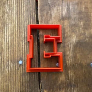 May include: Orange plastic cookie cutter shaped like the letter E.