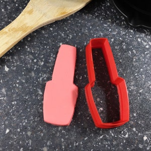 May include: A red plastic cookie cutter shaped like a nail polish bottle next to a pink nail polish bottle.