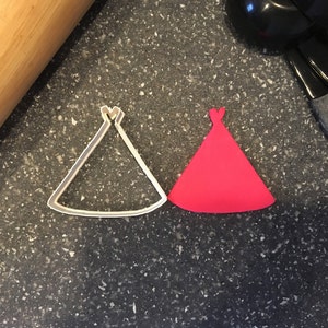 May include: A white plastic cookie cutter shaped like a pointed hat, and a red fondant cutout of the same shape.
