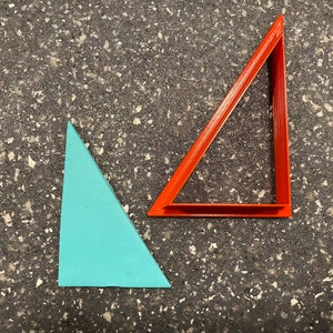 May include: Two triangles, one red and one light blue, are on a gray textured surface. The red triangle is a frame and the blue triangle is solid.