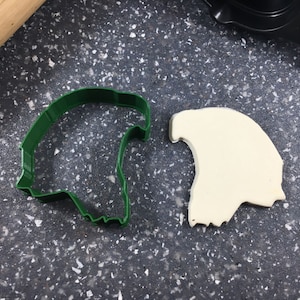 Pode incluir: Cortador de biscoitos de plástico verde em forma de caveira, ao lado de um recorte de massa de biscoito branca em forma de caveira.