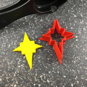 May include: Two star-shaped cookie cutters, one red and one yellow. The red cutter is larger and has a more intricate design.