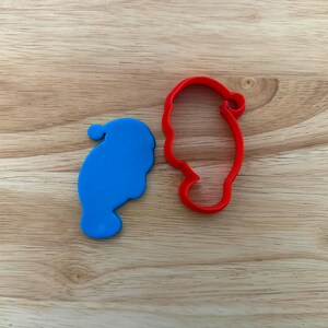 Peut inclure: Deux emporte-pièces en forme de bonnet de Père Noël, un bleu et un rouge, sont posés sur une surface en bois. Le bleu est plein, le rouge est un contour. Idéal pour la pâtisserie.
