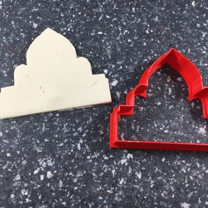 Può includere: Un tagliapasta di plastica rosso a forma di cupola con una cima appuntita. Il tagliapasta è su una superficie grigia macchiata.