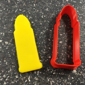 Pode incluir: Um cortador de biscoitos amarelo em forma de bala ao lado de um cortador de biscoitos vermelho em forma de bala.