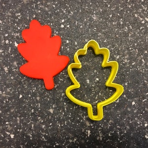 May include: Two leaf-shaped cookie cutters, one red and one yellow. The red cutter is solid, while the yellow cutter is hollow.