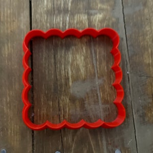 Może przedstawiać: Ciastko wykrawacz z czerwonego plastiku w kształcie kwadratu z falistymi krawędziami.