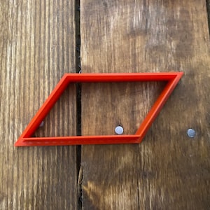 May include: A red plastic cookie cutter shaped like a parallelogram.