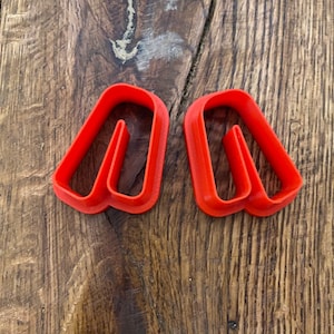 May include: Two red plastic cookie cutters shaped like the letter "A".