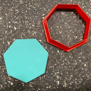 May include: A red octagonal cookie cutter and a light blue octagonal cookie cutter on a dark gray speckled surface.