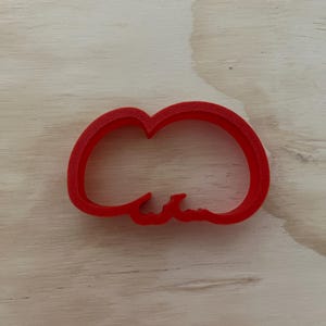 May include: Red plastic cookie cutter shaped like a cloud with a single, small, rounded protrusion on the bottom.