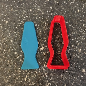 May include: A red plastic cookie cutter shaped like a lava lamp, next to a blue plastic lava lamp.