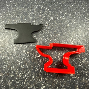 Puede incluir: Dos cortadores de galletas de metal con forma de yunque. Uno es negro y el otro es rojo.