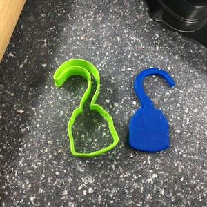 Pode incluir: Dois cortadores de biscoitos de plástico, um verde e outro azul, em forma de gancho de pirata.
