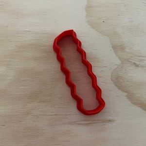 May include: Red plastic cookie cutter shaped like a candy cane with a wavy edge.