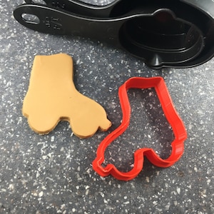 Puede incluir: Un cortador de galletas de plástico rojo en forma de patines y una galleta marrón en forma de patines.