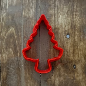 May include: Red plastic Christmas tree cookie cutter on a wooden background.
