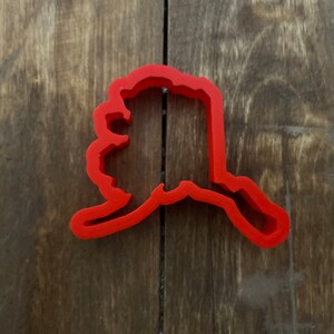 May include: Red plastic cookie cutter shaped like the state of Alaska.
