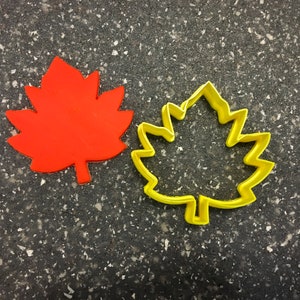 May include: Two leaf-shaped cookie cutters, one red and one yellow. The red cutter is solid, while the yellow cutter is an outline.