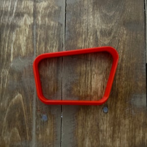 May include: A red plastic cookie cutter shaped like a rectangle with rounded corners.