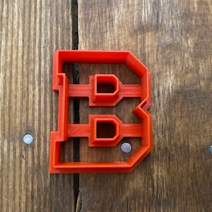 May include: A red plastic cookie cutter shaped like the letter B. The cookie cutter has a raised design and is perfect for making cookies or fondant.