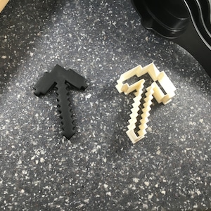 May include: Two cookie cutters in the shape of a pickaxe. One is black and the other is white.
