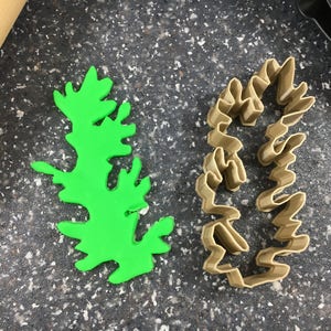 May include: Two cookie cutters, one green and one brown, shaped like a fern leaf.