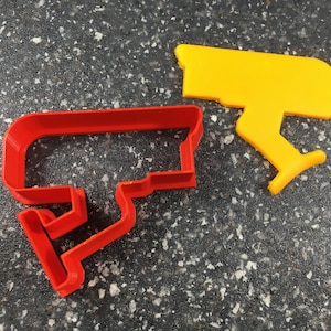 Puede incluir: Dos cortadores de galletas, uno rojo y otro amarillo, con forma de cámara de seguridad.