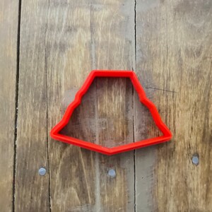 May include: Red plastic cookie cutter shaped like a Christmas tree. The cutter has a scalloped edge and a pointed top.