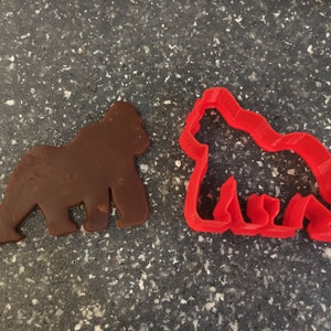 May include: A brown cookie cutter shaped like a gorilla next to a red plastic cookie cutter shaped like a gorilla.