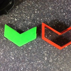 May include: Two arrow-shaped cookie cutters, one green and one red, on a grey speckled surface.