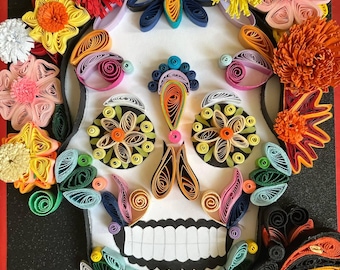 Könnte beinhalten: Ein farbenfrohes Papier-Quilling-Kunstwerk, das einen Zuckerschädel darstellt. Der Schädel ist mit leuchtenden Blumen in Rot-, Gelb-, Rosa- und Orangetönen verziert. Das Design umfasst einen Schmetterling und komplizierte Details.