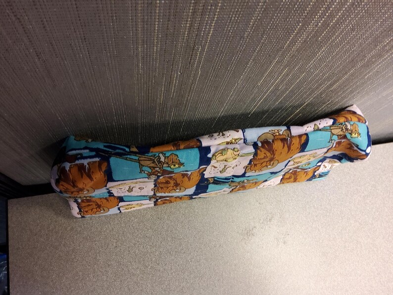 May include: A long, rectangular, blue, pink, and brown fabric pillow with a cartoon pattern. The pillow is lying on a light brown surface.