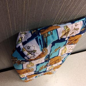 May include: A blue and white fabric pouch with a brown, blue, and white pattern of cartoon characters. The pouch is folded and lying on a gray surface.