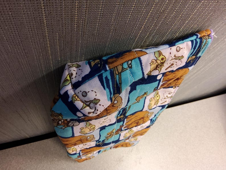 May include: A blue and white fabric pouch with a brown, blue, and white pattern of cartoon characters. The pouch is folded and lying on a gray surface.