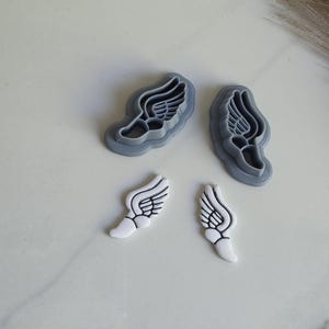 May include: Two gray plastic cookie cutters shaped like winged feet, and two white cookie cutters shaped like winged feet.