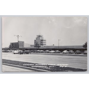 May include: A black and white vintage postcard showing General Mitchell Field Airport in Milwaukee, Wisconsin. The scene features a multi-story control tower, a long terminal building, and a parking lot filled with mid-century automobiles.