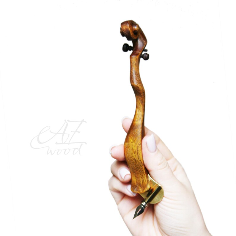 Puede incluir: Una pluma de caligraf&iacute;a de madera con un mango curvo &uacute;nico y una punta de oro. La pluma se sostiene en una mano, mostrando su tama&ntilde;o y forma.
