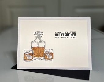 以下が含まれることがあります： デカンタとウイスキーグラス2つが描かれた白いカード。カードには「Sending you an Old-Fashioned Birthday Card.」と書かれています。