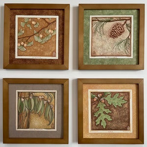May include: Four framed prints with botanical illustrations of different trees. The prints are in wooden frames with a light brown finish. The prints feature a ginkgo tree, a pine cone, a eucalyptus tree, and an oak tree. Each print has the name of the tree written below the illustration.