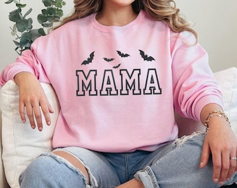 May include: A light pink sweatshirt with the word "MAMA" in black block letters and black bat silhouettes above. The sweatshirt is a crew neck style.