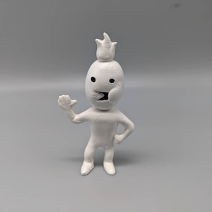 May include: White figurine of a person with a crown on their head. The figurine has a simple, cartoon-like design and is standing with one arm raised.