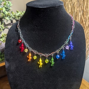May include: A silver chain necklace with rainbow colored beads and small figurines hanging from it. The necklace is displayed on a black mannequin.