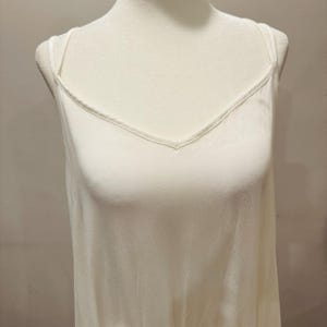 Puede incluir: Una camisola color crema con cuello en V y tirantes finos. La tela parece suave y cae suelta. La camisola se exhibe en un maniqu&iacute;, mostrando su dise&ntilde;o y ajuste. El dobladillo inferior tiene un delicado ribete.